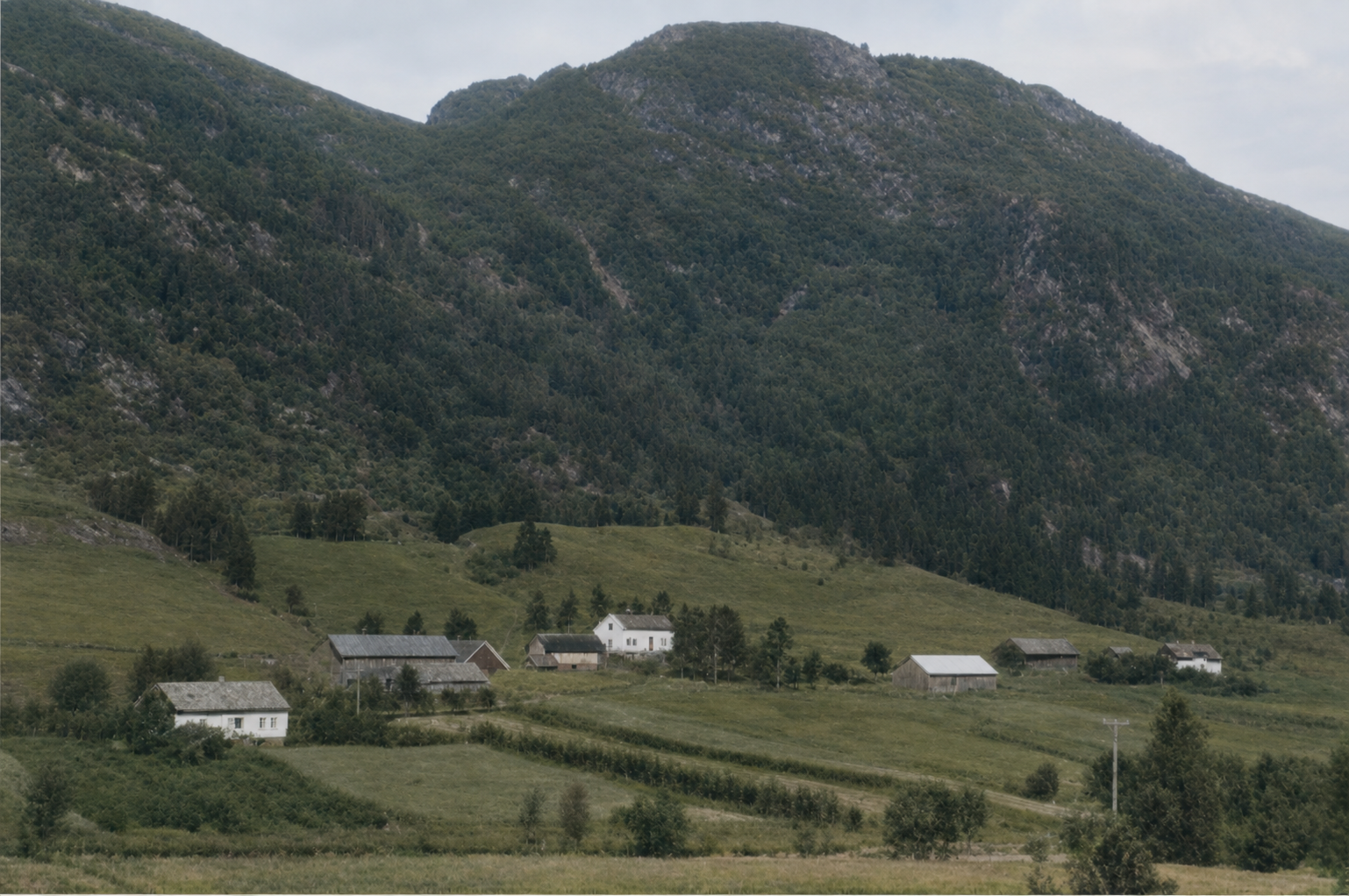 Tynning gården i Brekke, Sogn, liggende i grønne lier med fjell i bakgrunnen